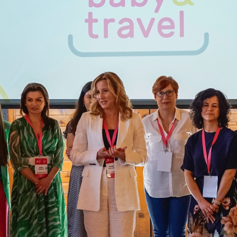 Sześć kobiet stoi przed ekranem wyświetlającym "baby & travel" podczas wydarzenia Klockomania w kwietniu 2024 roku. Jedna z nich, ubrana w biały garnitur, przemawia, podczas gdy pozostałe słuchają, tworząc profesjonalną atmosferę wydarzenia.